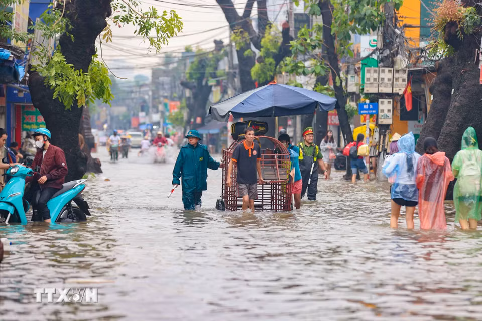 Lực lượng công an phường đã lắp đặt nhiều điểm cảnh báo nguy hiểm, liên tục hỗ trợ người dân di chuyển trên đường ngập được an toàn. (Ảnh: Thanh Tùng/TTXVN)