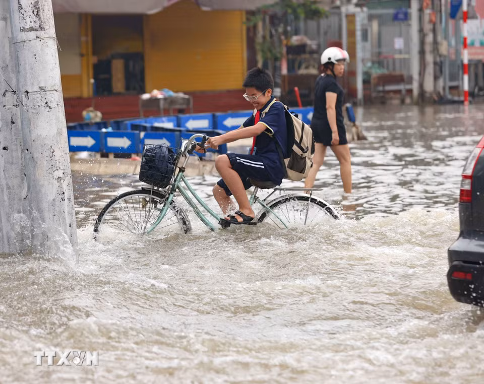 Học sinh đi học về qua đường Tây Mỗ đang bị ngập. (Ảnh: Thanh Tùng/TTXVN)