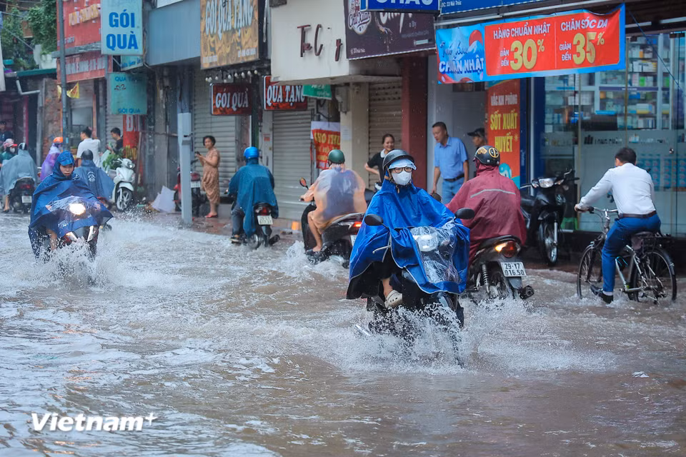 Người dân men theo vỉa hè di chuyển để tránh đoạn ngập nước sâu. (Ảnh: Hoài Nam/Vietnam+)