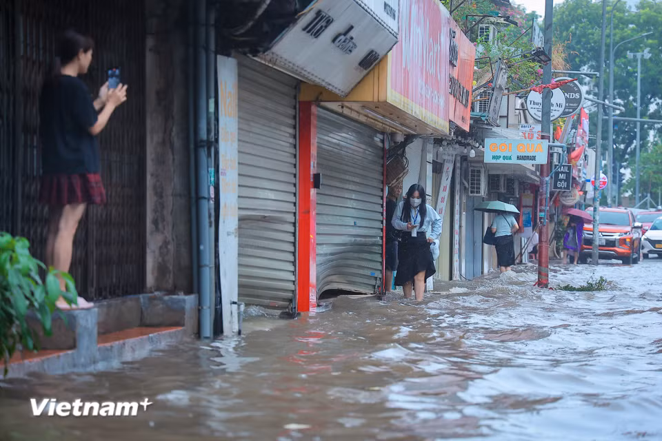 Người dân men theo vỉa hè di chuyển để tránh đoạn ngập nước sâu. (Ảnh: Hoài Nam/Vietnam+)