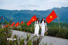 Hai nữ sinh trong trang phục áo dài giữa không gian rực rỡ cờ Tổ quốc trên cánh đồng Mường Thanh. (Ảnh: Xuân Tư/TTXVN)