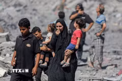 Người dân Palestine đứng trên đống đổ nát sau các cuộc không kích của Israel xuống Dải Gaza. (Ảnh: IRNA/TTXVN)