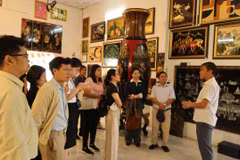 Khách tham quan lắng nghe giới thiệu về lịch sử tranh sơn mài tại cơ sở sản xuất sơn mài Định Hoà. (Ảnh: Khánh Ly/Vietnam+)