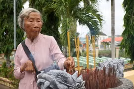Bà Đặng Thị Bảy thắp hương cho đồng đội đang yên nghỉ tại Nghĩa trang liệt sĩ xã Long Hưng A. (Ảnh: Nhựt An/TTXVN)
