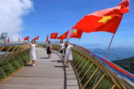 Giới trẻ thích thú được check-in trên Cầu Vàng với dãy cờ Tổ quốc tung bay. (Ảnh: Trần Lê Lâm/TTXVN)