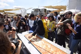 Nhân viên của Sách kỷ lục Guinness đo chiều dài chiếc bánh pizza tại Hội chợ triển lãm EXPO ở Milan. (Ảnh: AFP/TTXVN)