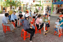 Nhiều phụ huynh ôm con ngồi sân trường bức xúc vì con mình không được nhận vào lớp học. (Ảnh: Phan Quân/TTXVN)
