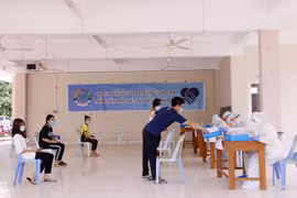 Các sinh viên Việt Nam nộp giấy khai tên họ, số điện thoại và khai lịch sử đi lại cho các nhân viên y tế Lào trước khi lấy mẫu xét nghiệm. (Ảnh: Phạm Kiên/Vietnam+)