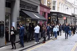 Người dân xếp hàng mua đồ bên ngoài một cửa hàng ở London (Anh). (Ảnh: AFP/TTXVN)