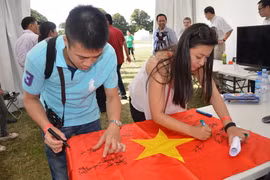 Sinh viên ký tên lên lá cờ Tổ Quốc, thể hiện tình yêu và trách nhiệm đối với quê hương đất nước. (Ảnh: Bích Hà/Vietnam+)