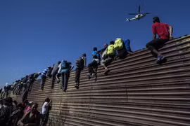 Người di cư vượt qua hàng rào biên giới giữa Mỹ và Mexico, gần cửa khẩu El Chaparral ở Tijuana, bang Baja California, Mexico ngày 25/11/2018. (Ảnh: AFP/TTXVN)