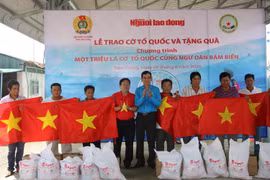 Chủ tịch Liên đoàn lao động tỉnh Tiền Giang Trương Văn Hiền và Tổng Biên tập Báo Người Lao động Tô Đình Tuân trao quà và cờ Tổ quốc cho các ngư dân có hoàn cảnh khó khăn. (Ảnh: Hữu Chí/TTXVN)