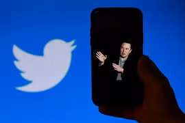 Chân dung tỷ phú Elon Musk trên màn hình điện thoại và biểu tượng Twitter (phía sau). (Ảnh: AFP/TTXVN)