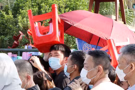 Một người xếp hàng mua vé dùng ghế để che nắng, chờ đến lượt được mua vé. 