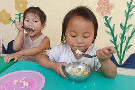 Bữa ăn bán trú của học sinh điểm trường Sáng Xoáy. Không có điện, để thoáng mát, các em ăn bữa trưa ở ngay hàng lang lớp học. (Ảnh: Phạm Mai/Vietnam+)