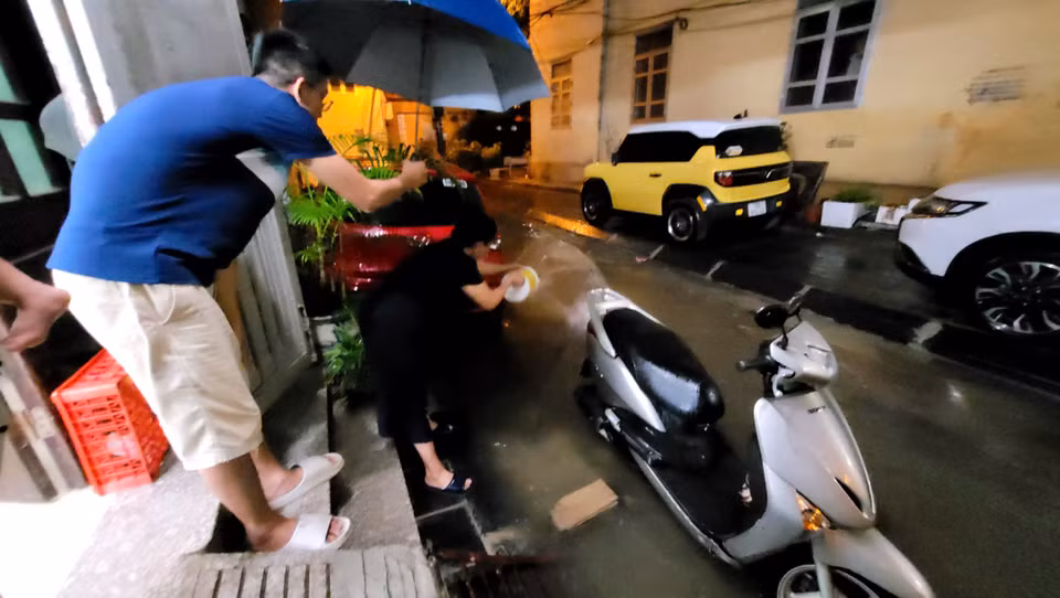 Một số gia đình chủ động tạt nước, thông miệng cống để giảm thiểu ngập úng trong ngõ. (Ảnh: Minh Anh/Vietnam+)
